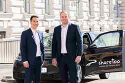 Zwei Männer (Steffen Gersch, Geschäftsführer Porsche Mobility, und Dominik Grimm, Head of Business Development sharetoo/Porsche Mobility)  in Anzug stehen vor einem sharetoo VW und schauen in die Kamera.