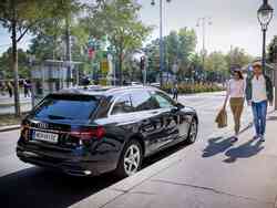 Eine Frau und ein Mann Alters gehen an der Beifahrer-Tür eines schwarzen AUDI Kombis vorbei